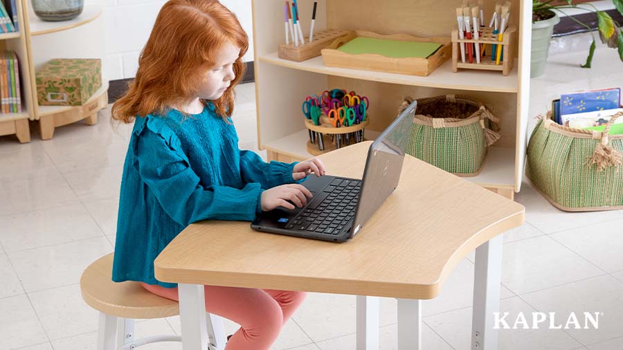 A young child sits at a Sense of Place for Elementary desk, a laptop computer is open in front of the child. 