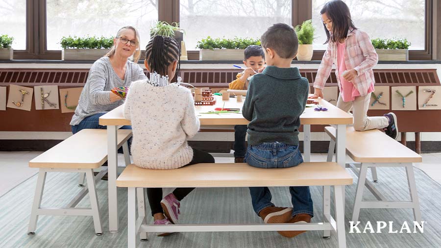 An early elementary teacher sits at a Sense of Place for Elementary collaboration table with four students. They are working on a creative project as a small group. 