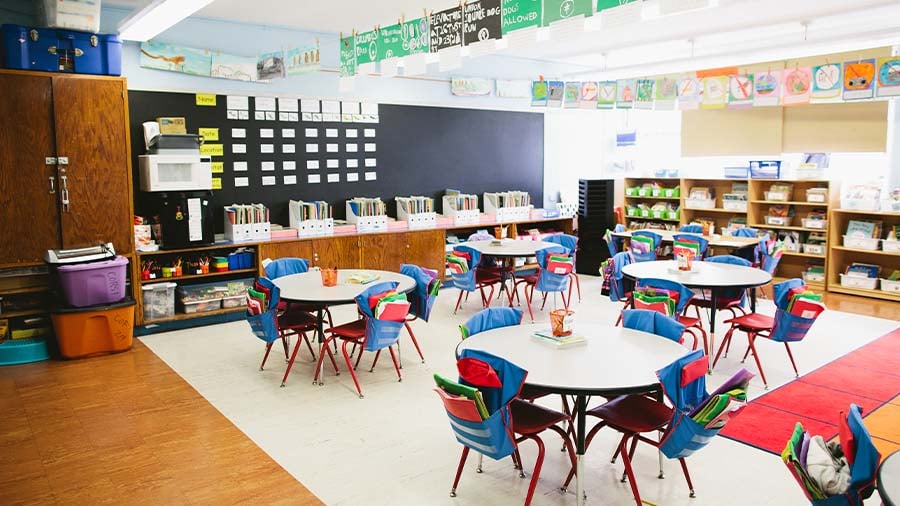 An image of an early elementary classroom featuring tables, chairs, and learning materials. 