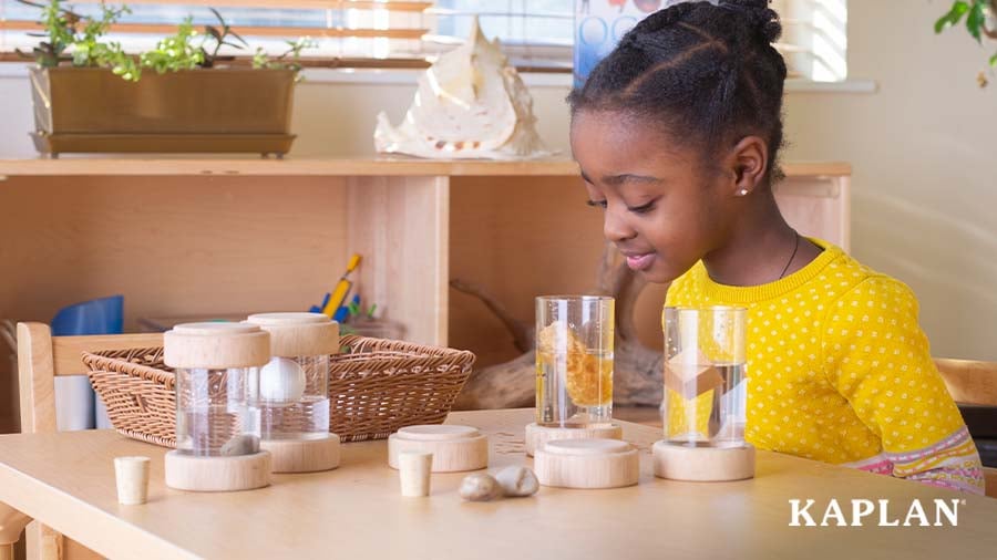 A young girl in a yellow shirt looks down at a clear tube which holds a sponge and water. 