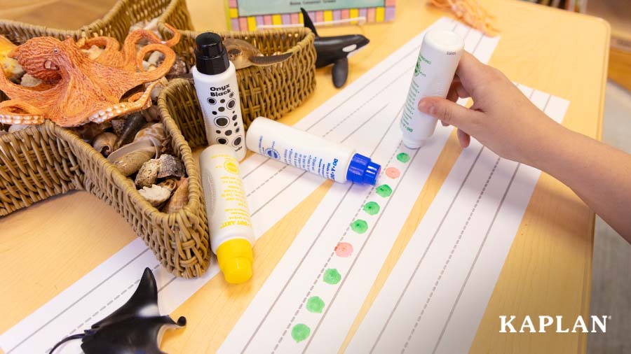 An image of a young child's hand holding a paint dauber and creating colorful patterns on a paper sentence strip. 