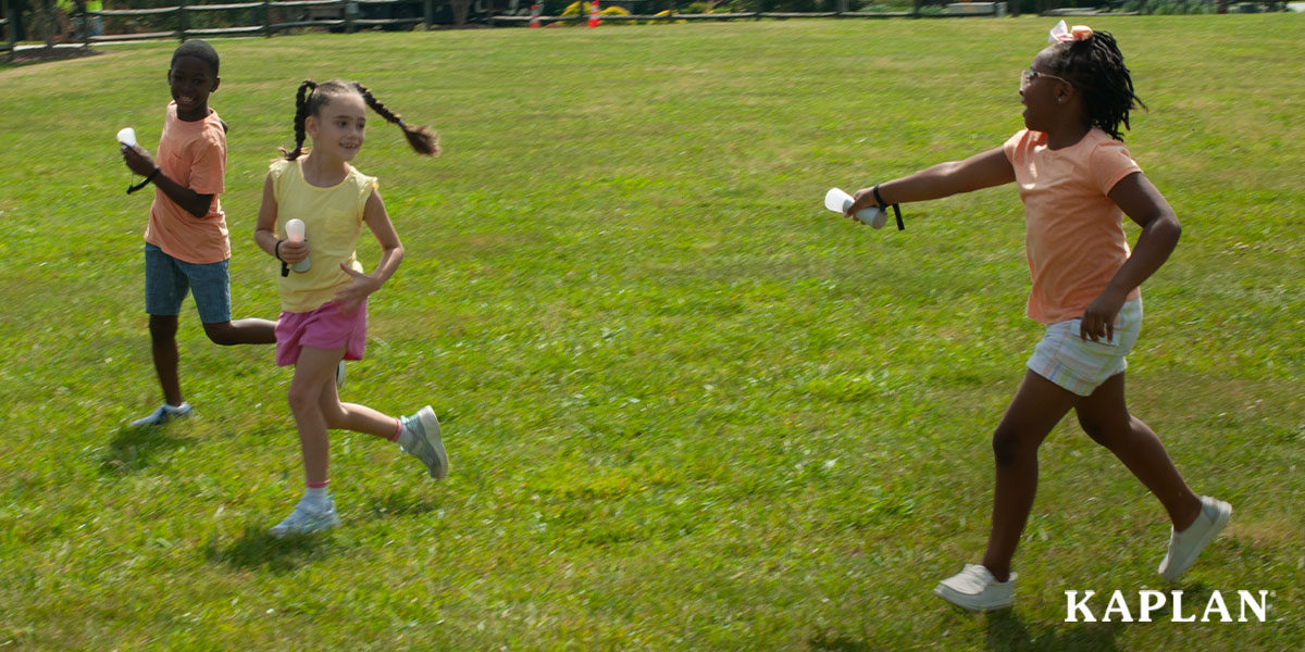 A group of three children, each holding a Picoo gaming wand, run in an open grassy area while playing a game on the Picoo.
