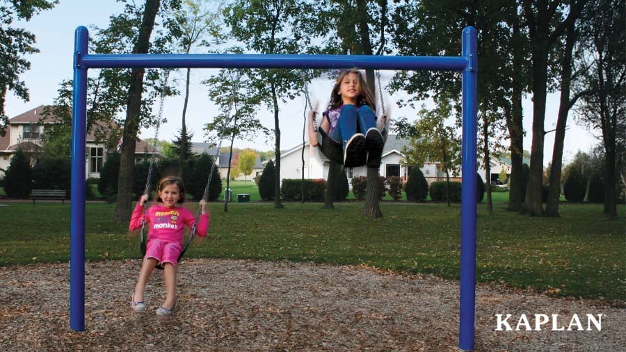 Two young girls are using the swings on an outdoor play structure. The girls are looking at the camera and smiling. 