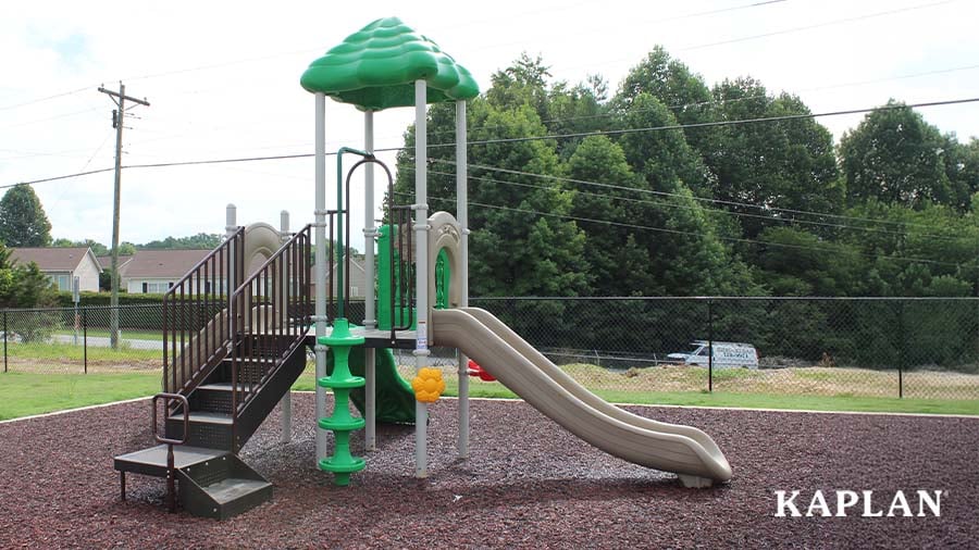 An image of a second green and tan outdoor play structure that features multiple platforms, two slides, and a climbing pole. 