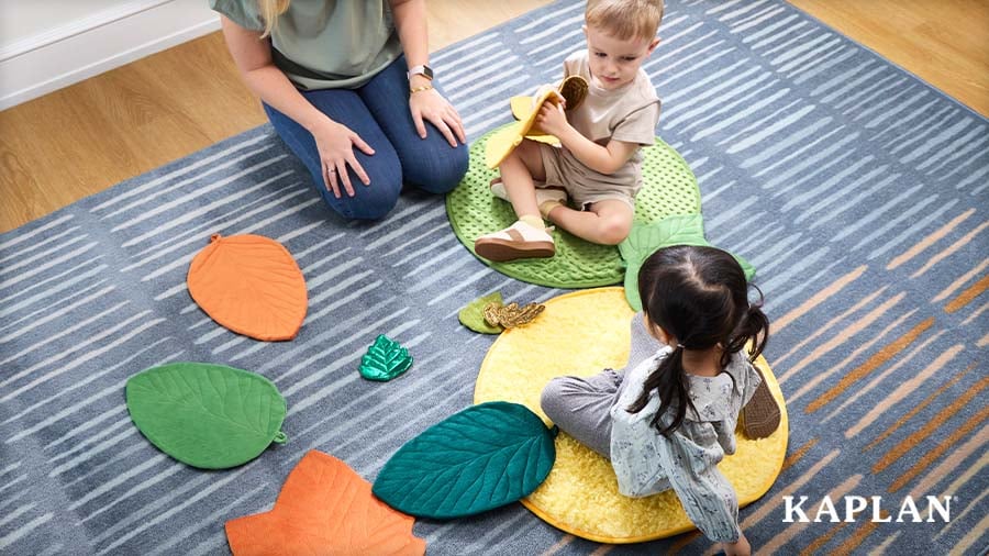 Educator and two young children sitting on colorful leaf-shaped floor cushions during a group activity