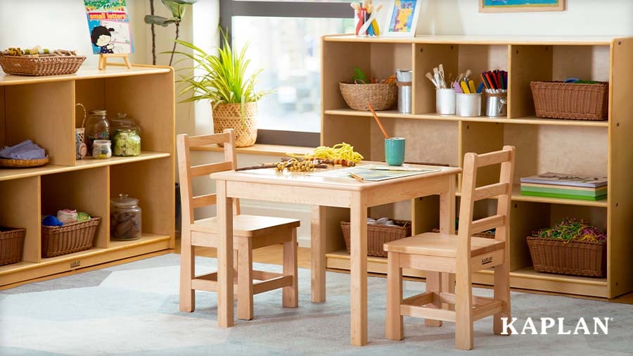 Cozy early childhood classroom corner with a low wooden table, open shelving, wicker baskets, and natural light