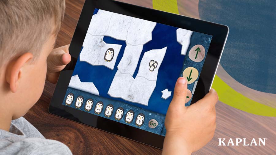 A young boy looks down at a tablet, on the screen is an image from the Precoding Penguins app. 