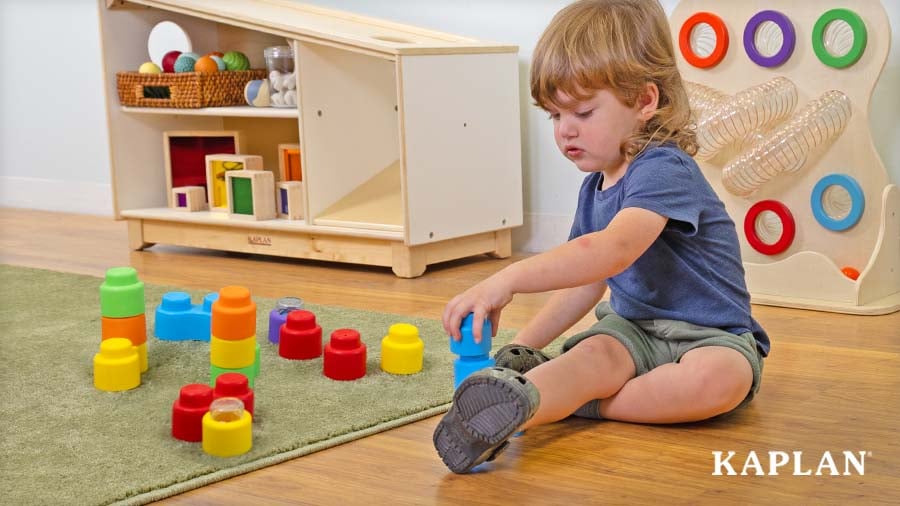 Preschooler stacking blue Happy Sound & Animal Soft Blocks on the classroom carpet