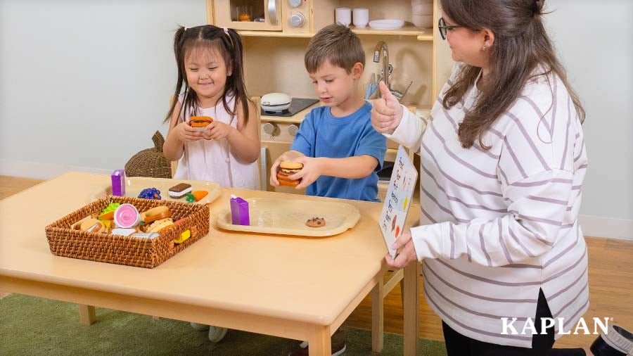 Two young children build pretend sandwiches with the New Sprouts Super Sandwich Set as an adult guides them