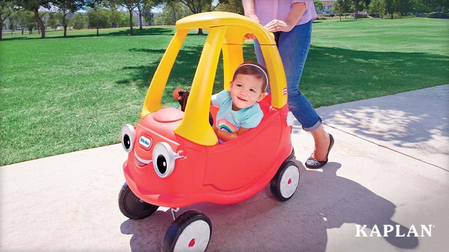 A smiling toddler riding inside a Cozy Coupe Car as an adult pushes from behind