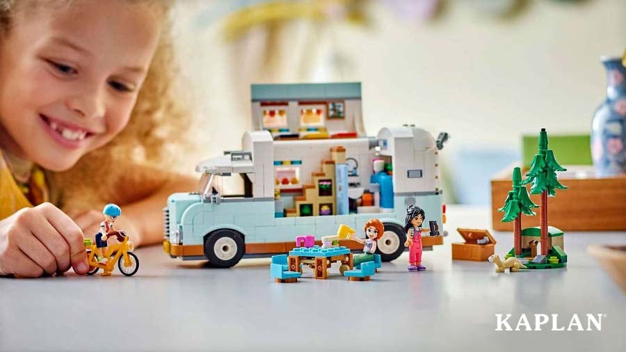 Smiling child playing with a LEGO Friends Friendship Camper Van Adventure set with mini-figures, a bike, and picnic table