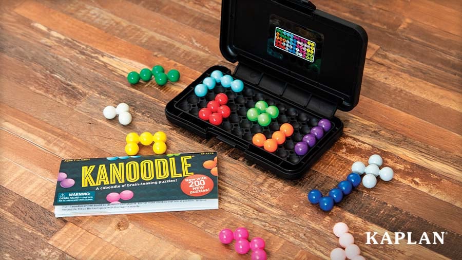 Kanoodle puzzle game with colorful bead pieces in a black case, beside the instruction booklet on a wooden floor