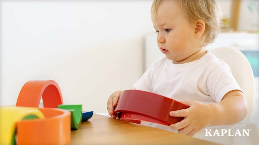 Toddler exploring colorful wooden rainbow stacking arches at a classroom table