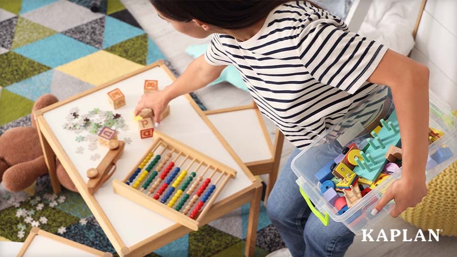 Young child cleaning up blocks, puzzle pieces, and loose parts from classroom table