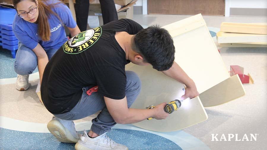Two Kaplan employees assembling a wooden play kitchen unit