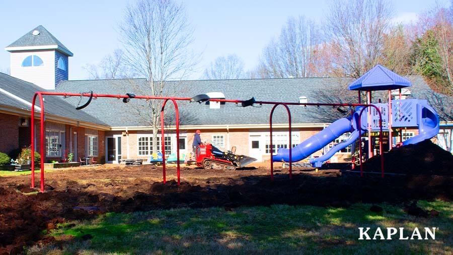 An image of the playground installation process featuring a Bobcat tractor grading the land near a large blue metal playset. 