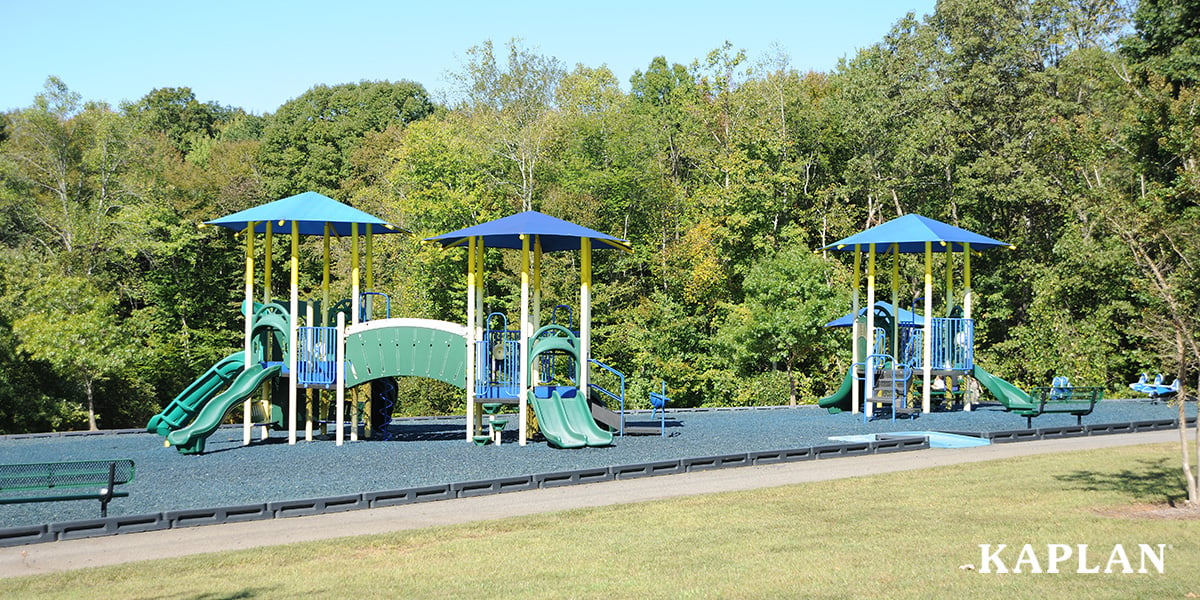 Featured image: Two blue and green playground structures in front of green leafy trees on a sunny day. - Read full post: How Much Does a Preschool Playground Cost?
