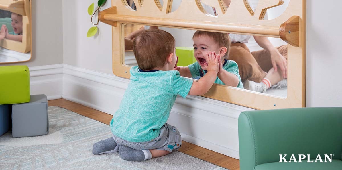 Featured image: A young infant in a blue shirt sits on the floor, staring at his reflection in a mirror which is attached to the wall in front of him.  - Read full post: Mirror Magic: Using Reflective Surfaces in the Early Childhood Classroom