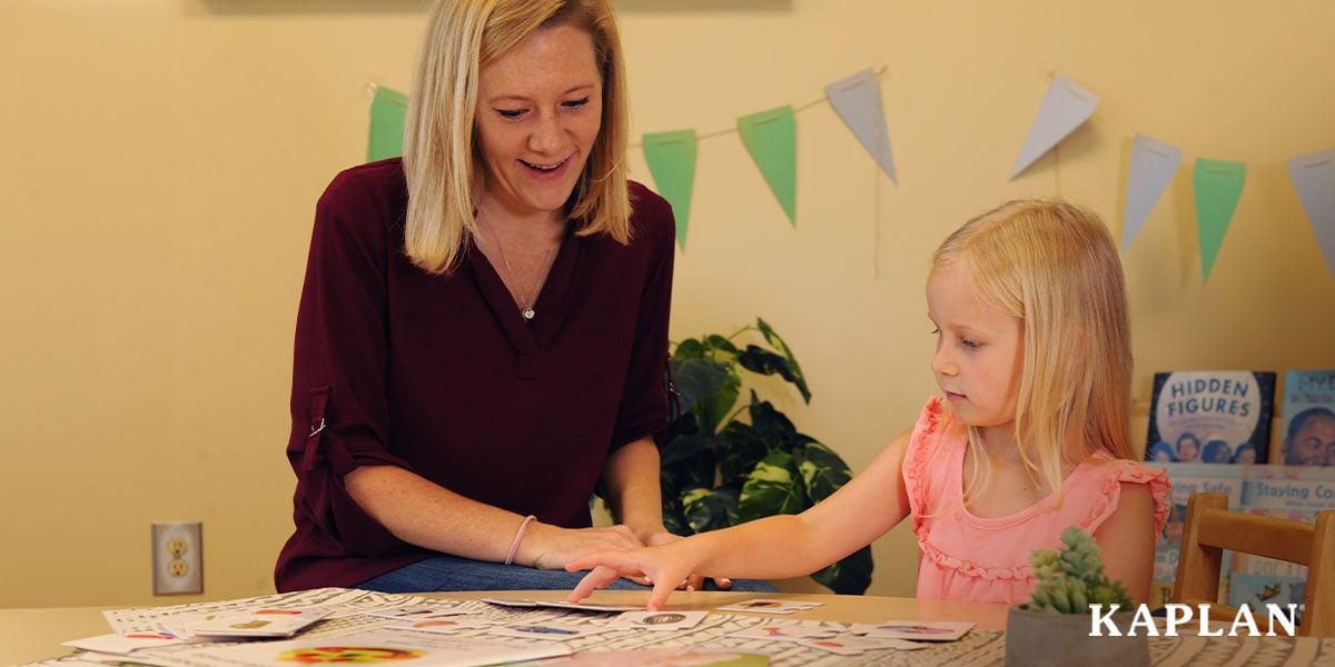 Featured image: An early childhood teacher sits beside a young child at a table in an early childhood classroom. On the table are flash cards, the child is reaching out to touch one of the cards.  - Read full post: 4 Factors That Affect Your Resilience as an Early Childhood Professional