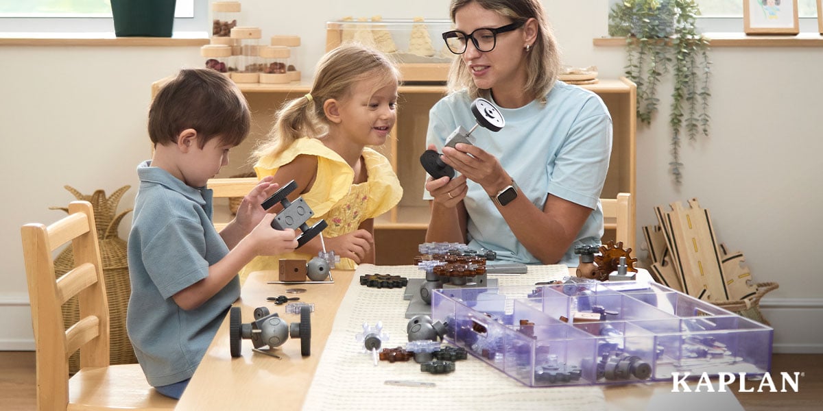 Featured image: Early childhood educator shows a wheel piece as two preschoolers assemble gray construction vehicles - Read full post: 4 Powerful Benefits of Loose Parts Play in 2026