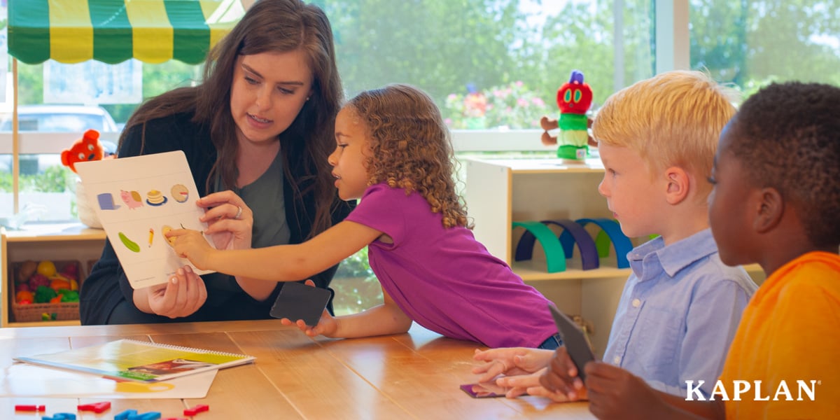 Featured image: An early childhood teacher shows children image flash cards while sitting at a wooden table.  - Read full post: A Complete Look at Nemours Children’s Reading BrightStart!