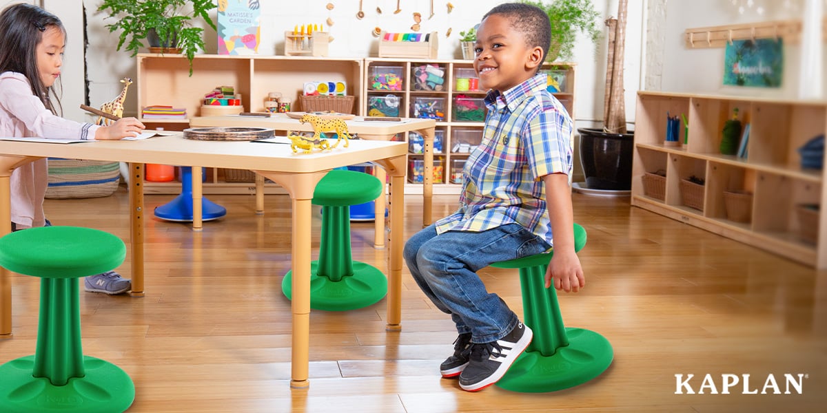 Featured image: Young child sits and smiles on a green wobble stool as another child works at a nearby table - Read full post: How to Successfully Introduce Flexible Seating in the Classroom