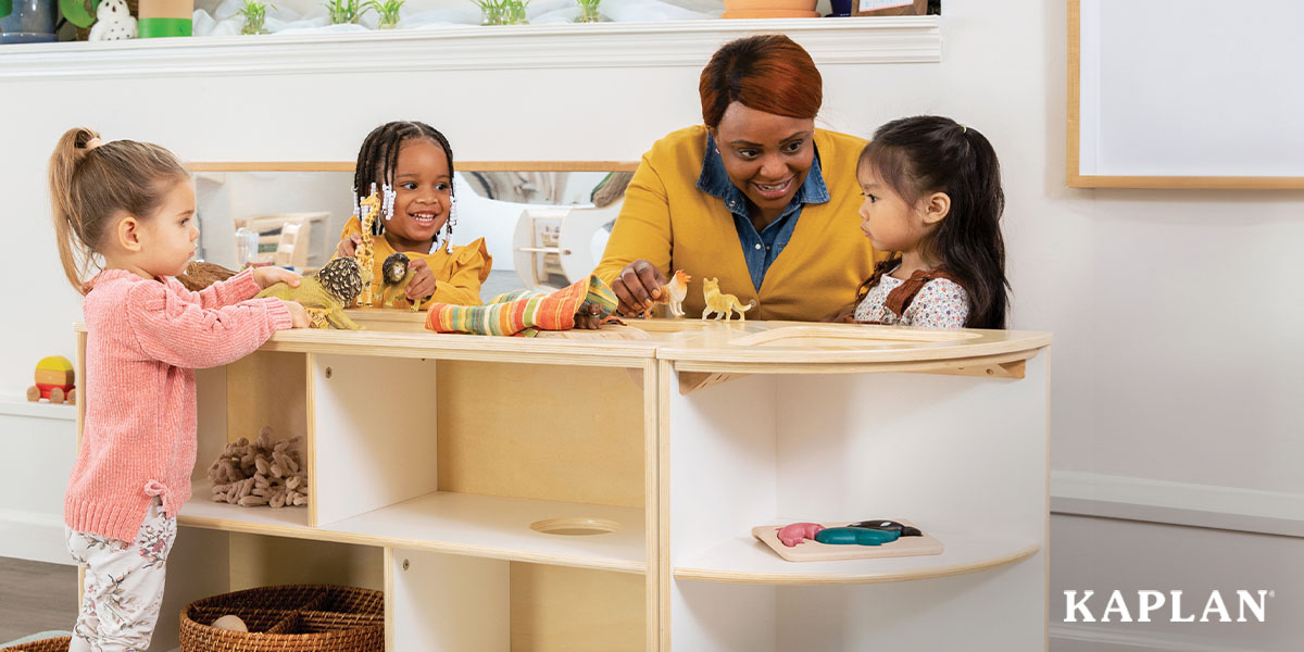 Featured image: An early childhood teacher sits at a Sense of Place Wee Ones Shelving Unit, she is holding a toy animal in her hand while smiling at a young child to her left. Two more child are at the teachers right, also smiling and holding toy animals in their hand.  - Read full post: Maryland EXCELS Bonuses: New Funding For Early Childhood Programs