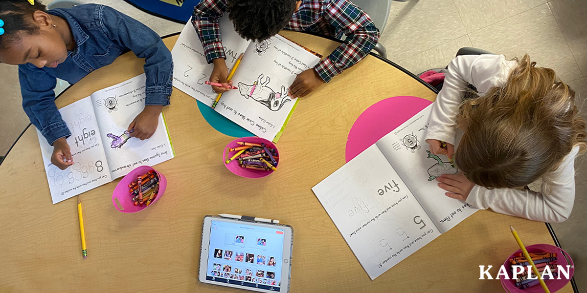 Featured image: Three children sit at wooden table, the each have a My Math alive Student Journal open in front of them on the table. Each child is marking in the journal with a crayon while looking at the pages.  - Read full post: Improve Learning Outcomes with 3D Augmented Reality Preschool Workbooks